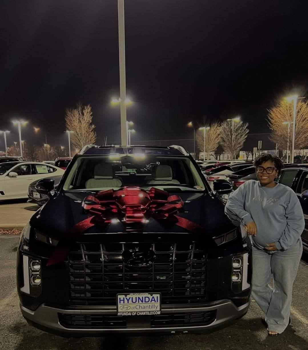 Woman standing next to new car with big red bow on the hood.